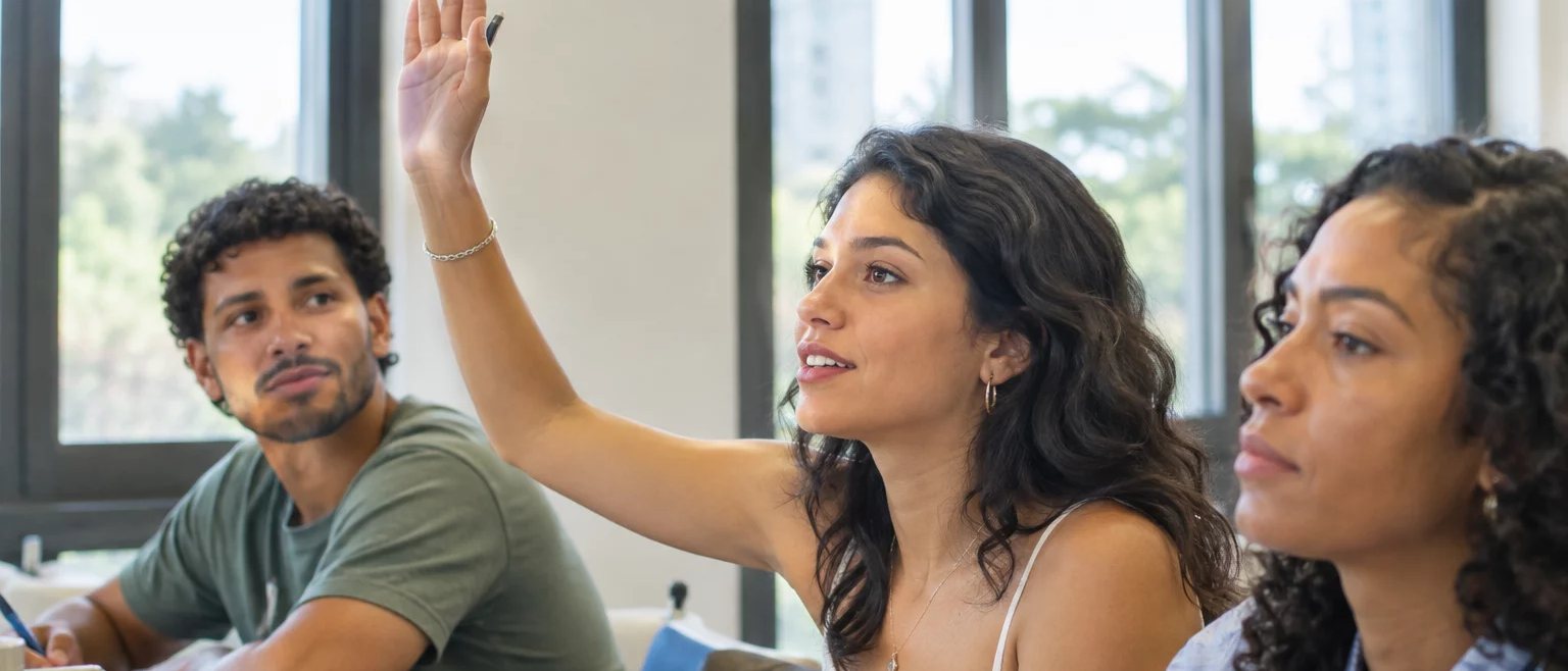 Participante com a mão erguida pedindo a vez, à mesa coberta de folhas escritas